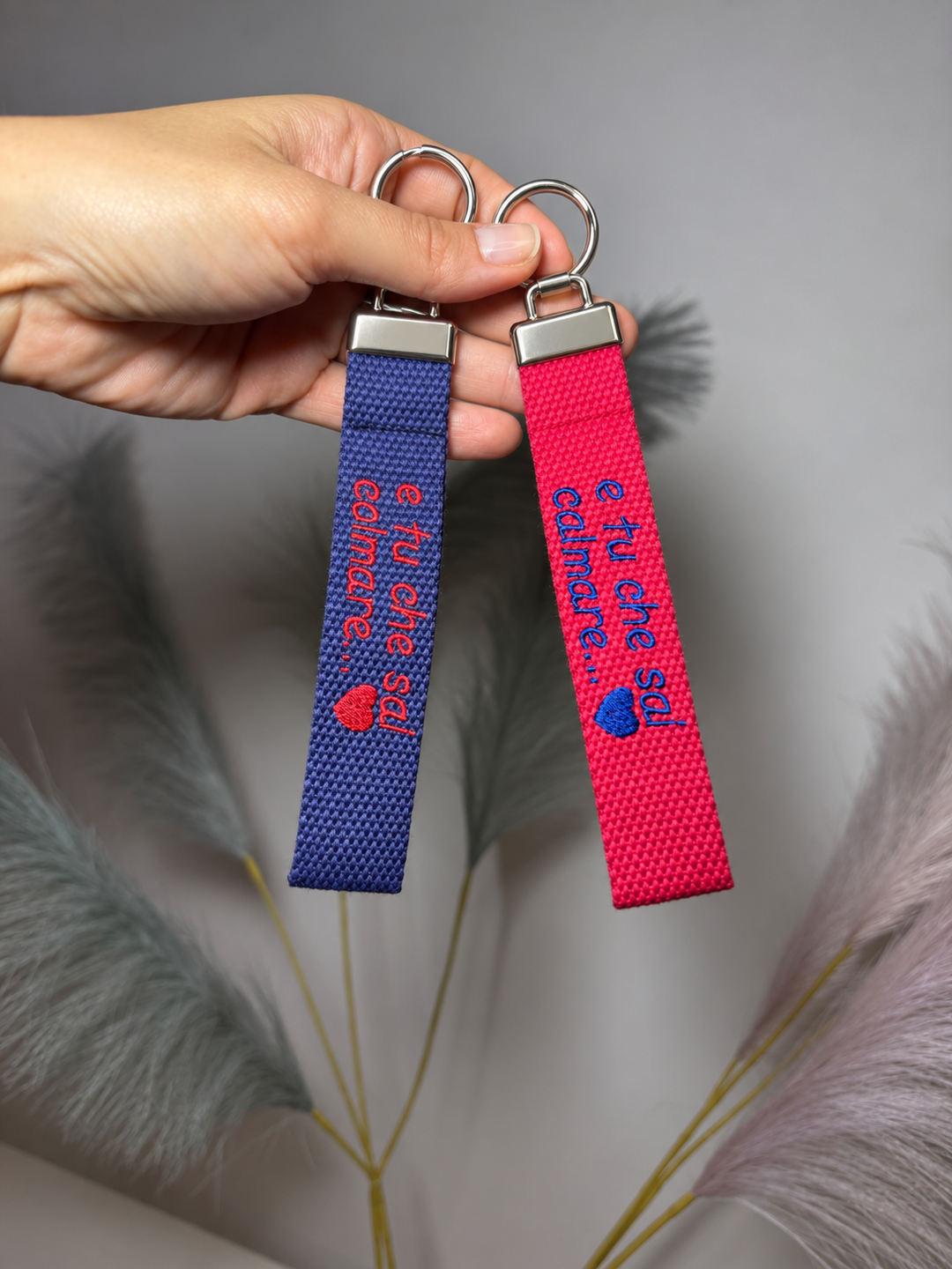 Portachiavi in tela blu e fucsia con ricamo personalizzato tenuti in mano
