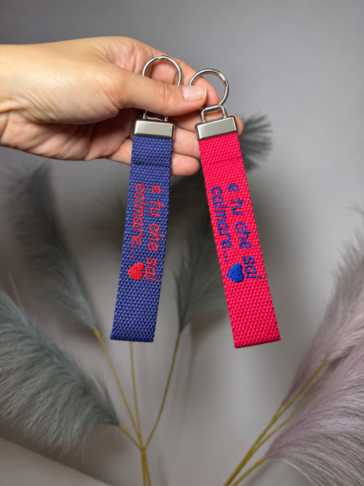 Portachiavi in tela blu e fucsia con ricamo personalizzato tenuti in mano