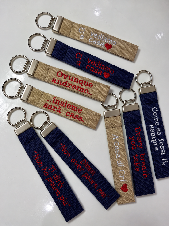 Portachiavi personalizzati in tela beige, blu e rosa con frasi ricamate e cuore rosso, disposti insieme