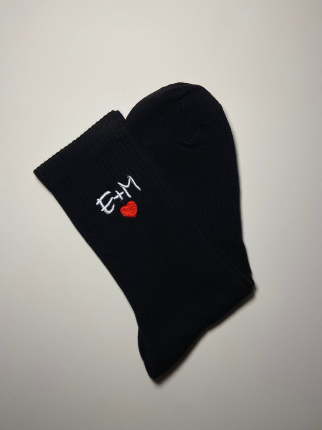 Calzini sportivi personalizzati neri con iniziali ricamate bianche e cuore rosso. Ideali per un tocco unico e originale nel tuo outfit sportivo.