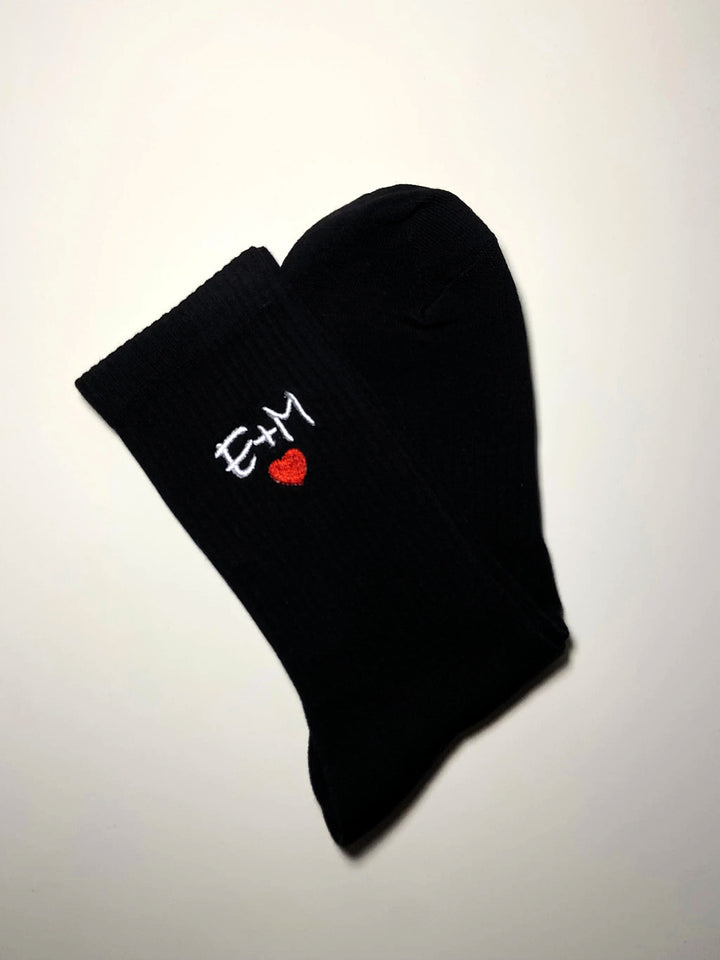 Calzini sportivi personalizzati neri con iniziali ricamate bianche e cuore rosso. Ideali per un tocco unico e originale nel tuo outfit sportivo.