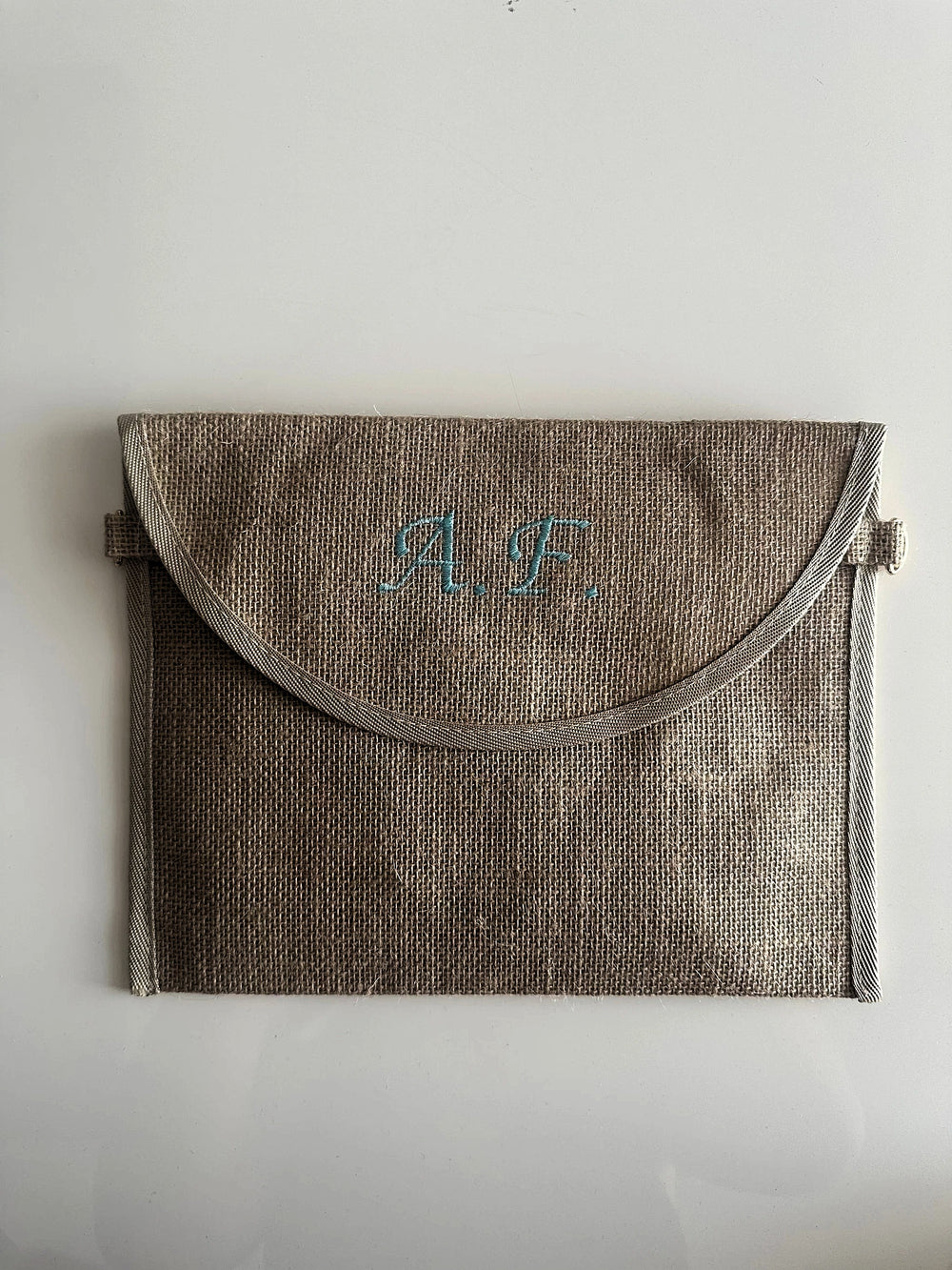 Pochette in juta personalizzata con iniziali  ricamate in azzurro, ideale come borsa elegante e sostenibile per ogni occasione.