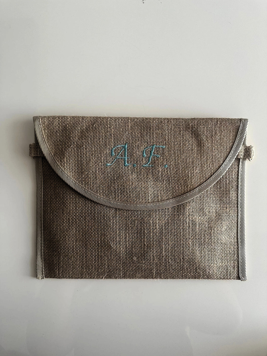 Pochette in juta personalizzata con iniziali  ricamate in azzurro, ideale come borsa elegante e sostenibile per ogni occasione.