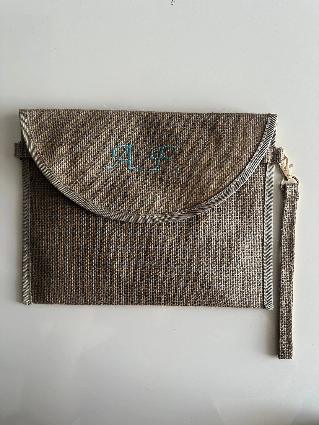Pochette in juta personalizzata con iniziali, chiusura a patta e cinturino laterale, ideale come borsa elegante e sostenibile.